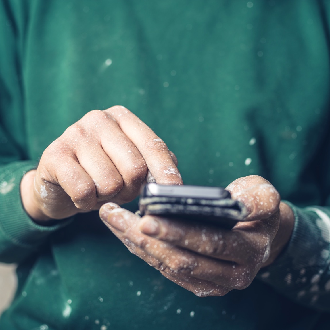 Image of hands covered in paint splatter using a smartphone to look something up